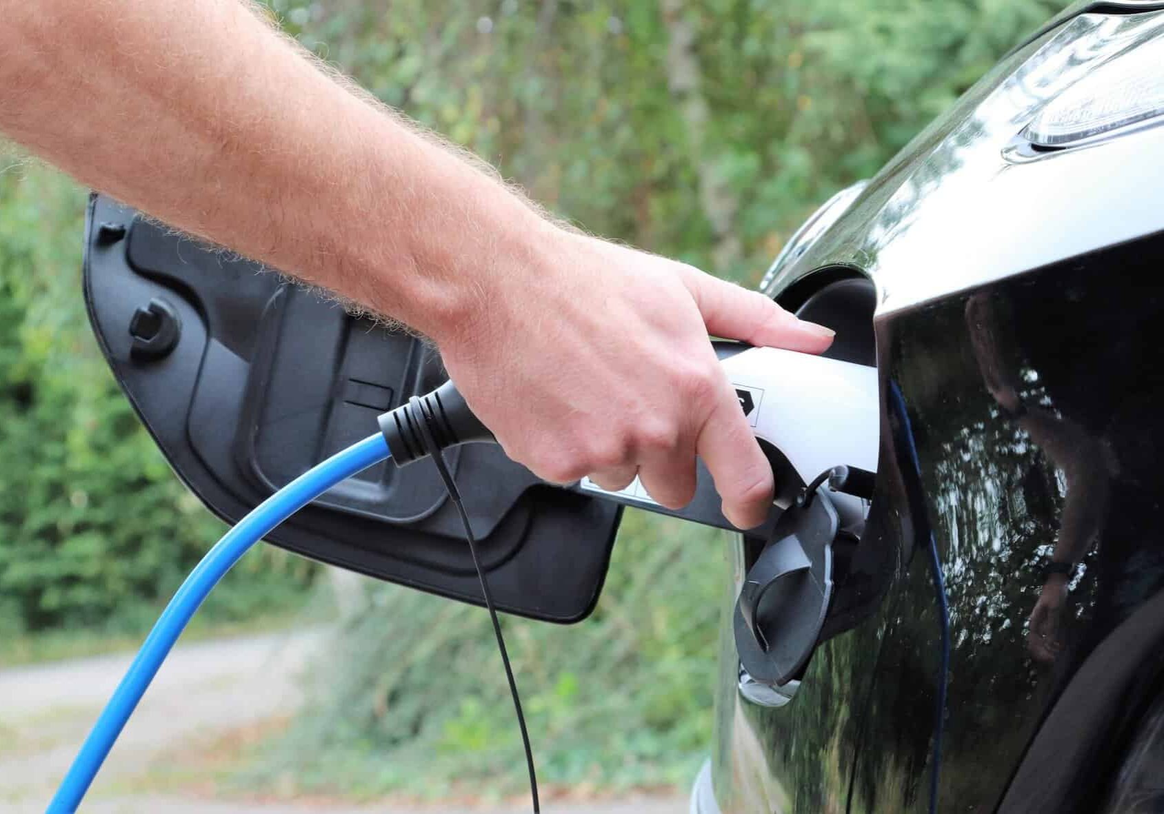Using a blue cable, a person charges an EV (electric vehicle).