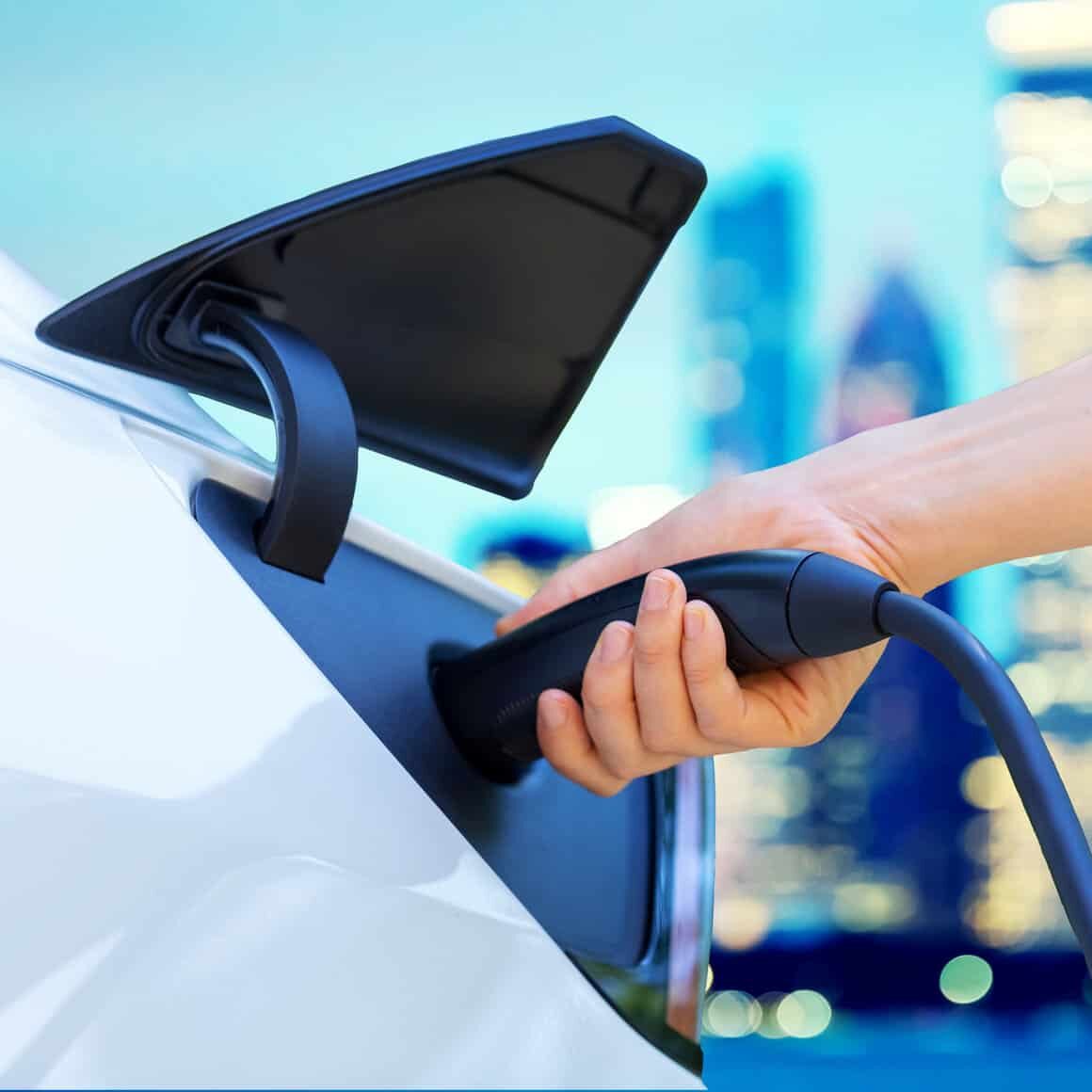 A person is GOEV charging an electric car in front of a city.